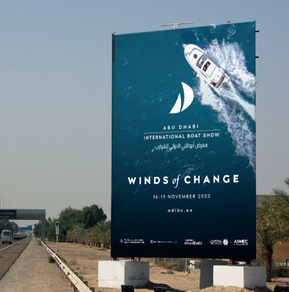 Valla publicitaria junto a una carretera con una fotografía de yate, el logotipo del evento y el lema "Winds of Change"