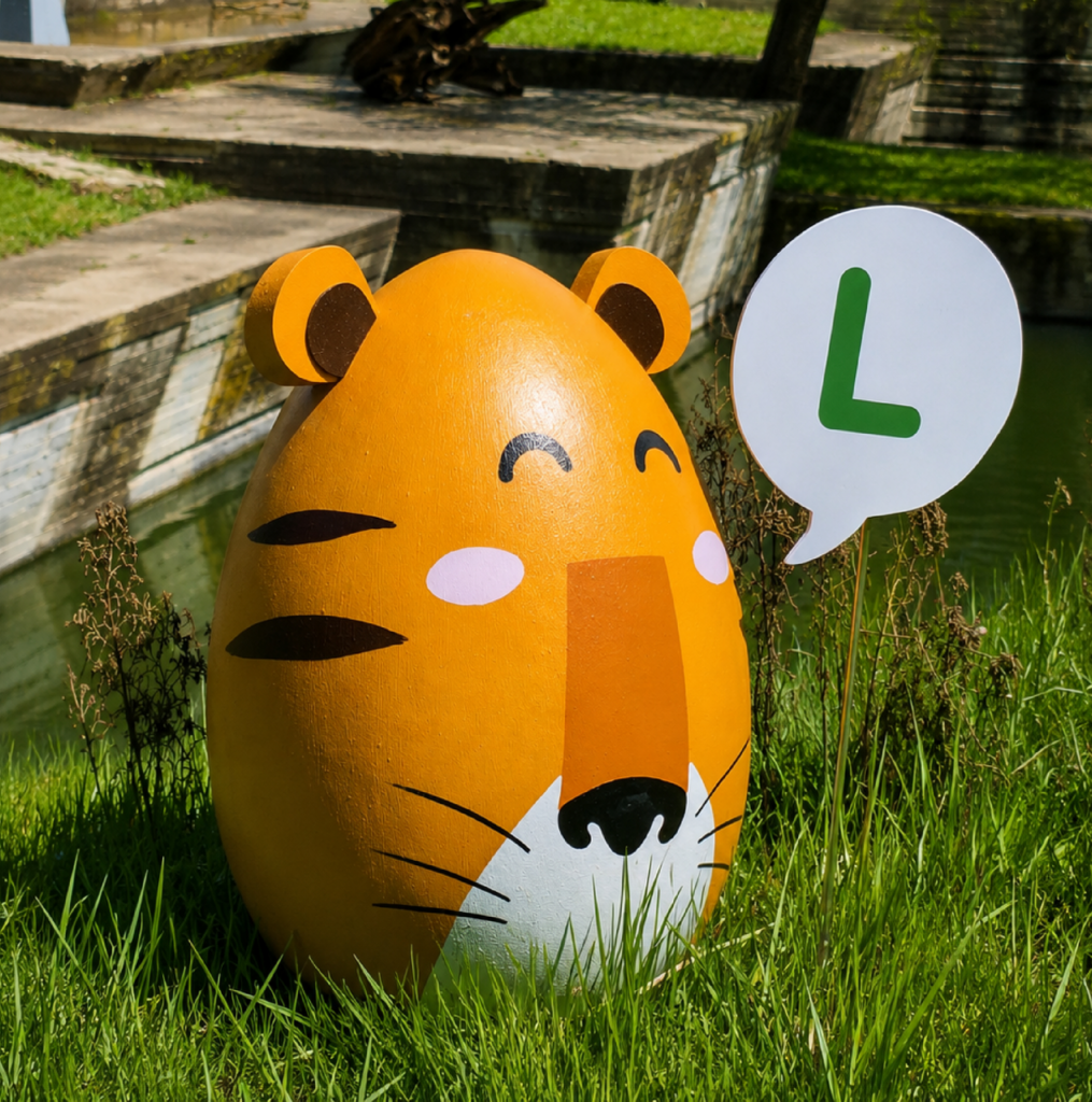 Huevo escultórico con forma de tigre entre la hierba, con un cartel con la letra L